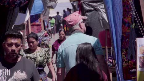 Old-man-gringo-walking-through-Chichi-market-in-Guatemala,-uring-daytime