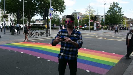 Un-Hombre-Guapo-Tomándose-Un-Selfie-Frente-Al-Cruce-Peatonal-Del-Arcoíris-En-Londres-Para-El-Mes-Del-Orgullo,-Toma-A-La-Altura-De-Los-Ojos,-Cámara-Estática,-Día,-Tiempo-Real