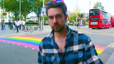 Hombre-Guapo-Preparándose-Para-El-Orgullo-Gay-Con-Gafas-De-Sol-Rosas-Frente-Al-Cruce-Peatonal-Del-Arco-Iris-En-Londres-Para-El-Mes-Del-Orgullo,-Toma-A-La-Altura-De-Los-Ojos,-Cámara-Estática,-Día,-Tiempo-Real,-Clasificación-De-Color