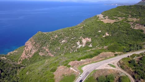 Toma-Aérea-De-Drones-Sobre-Una-Carretera-Costera-Con-Curvas-En-El-Mar-Azul-Mediterráneo,-Mientras-Los-Coches-Pasan-Por-La-Carretera