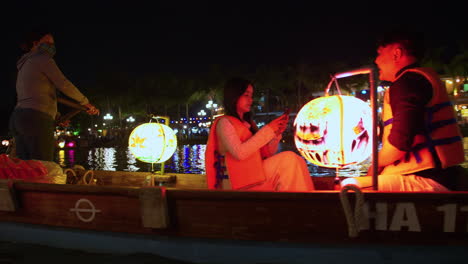 Una-Toma-De-Seguimiento-De-Turistas-Montando-Un-Colorido-Barco-Linterna-A-Lo-Largo-Del-Río-En-La-Ciudad-De-Hoi-An,-Vietnam