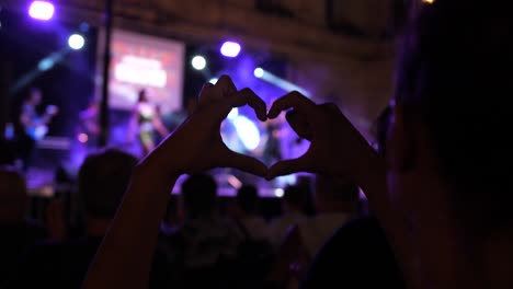 A-woman-in-the-audience-at-a-festival-raises-her-arms-and-makes-a-heart-shape-with-her-hands