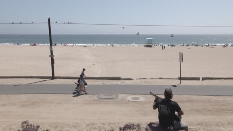 Hombre-Tocando-La-Guitarra-En-La-Playa-De-California-Con-Arena-Y-Océano-Al-Fondo