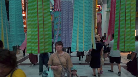 Gente-En-Arcade-Caminando-Entre-Serpentinas-De-Papel-Decorativas-Durante-El-Festival-De-Tanabata