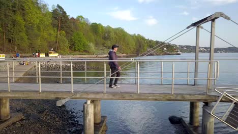 Toma-Lateral-De-Un-Turista-Caminando-Por-Un-Muelle-En-Nordstrand-Bad-Durante-La-Puesta-De-Sol-En-Oslo,-Noruega