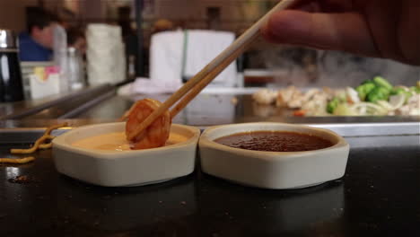 Nahaufnahme-Einer-Hand,-Die-Mit-Stäbchen-Garnelen-In-Soße-Taucht,-Neben-Einem-Teppanyaki-Grill-In-Einem-Japanischen-Restaurant