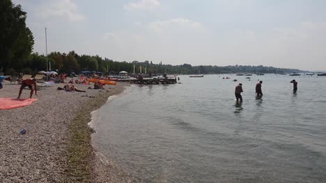 People-enjoying-their-leisure-time-on-a-beach-in-Lage-Garda-in-Northern-Italy,-on-a-warm-autumn-day