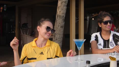 Un-Grupo-De-Mujeres-Sentadas-Y-Bailando-En-El-Bar-De-La-Playa-Disfrutando-De-Sus-Bebidas-Durante-El-Día