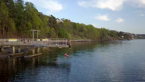 Rotating-Drone-Shot-of-a-person-sitting-at-the-end-of-the-pier-at-Nordstrand-Bad-in-Oslo,-Norway