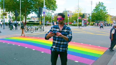 Un-Hombre-Guapo-Tomándose-Un-Selfie-Frente-Al-Cruce-De-Peatones-Del-Arcoíris-En-Londres-Para-El-Mes-Del-Orgullo,-Toma-A-La-Altura-De-Los-Ojos,-Cámara-Estática,-Día,-Tiempo-Real,-Color-Graduado