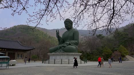 Gente-Caminando-Junto-A-Un-Gran-Buda-De-Bronce