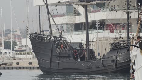 Ferdinand-Magellan-Nao-Victoria-carrack-boat-replica-with-spanish-flag-being-docked-in-Valencia-with-veles-e-vents-in-the-background-in-slow-motion-60fps