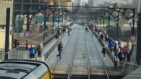 Einspielaufnahme,-U-Bahn-Straßenbahn-Fährt-Am-Bahnhof-An-Der-Don-Luis-I-Brücke-In-Porto,-Portugal-Vorbei,-Im-Hintergrund-Laufen-Menschen-Herum