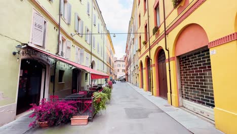 Young-couple-of-parents-walking-through-the-streets-of-Modena,-Emilia-Romagna-region,-Italy-with-empty-restaurants-like-Osteria-Ruggera-in-daytime,-clear-sky,-sparsely-populated-streets