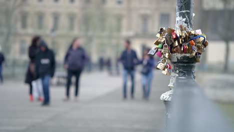 Clip-En-Cámara-Lenta-De-Candados-De-Amor-En-Un-Poste-En-El-Centro-De-La-Ciudad-De-París-Con-Gente-Caminando-Fuera-De-Foco-Borroso-En-El-Fondo