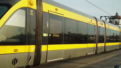 Zoom-Out-Slow-Motion-Shot,-Man-Driving-the-Metro-Tram-Train-Passing-by-at-Don-Luis-I-Bridge-in-Porto-Portugal