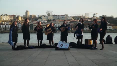 Toma-En-Cámara-Lenta,-Grupo-De-Jóvenes-Estudiantes-Tocando-Sus-Instrumentos-Y-Cantando,-El-Río-Duero-Al-Fondo