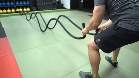 A-man-using-a-battling-rope-in-a-fitness-park-indoor-wearing-a-CrossFit-short