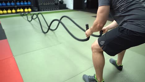 Un-Hombre-Usando-Una-Cuerda-De-Batalla-En-Un-Gimnasio-Cubierto-Usando-Un-Pantalón-Corto-De-Crossfit