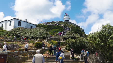 Faro-En-La-Cima-De-Una-Colina-En-Cape-Point,-Ciudad-Del-Cabo,-Sudáfrica,-Con-Gente-Subiendo-Las-Escaleras