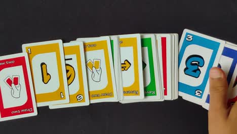 Overlay-panning-shot-of-male-hand-laying-out-Uno-cards-one-by-one-on-a-black-table