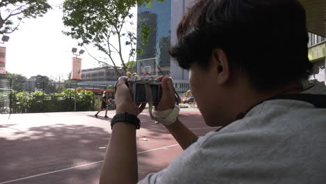 A-boy-adjusting-his-camera-taking-photos-at-a-basketball-court