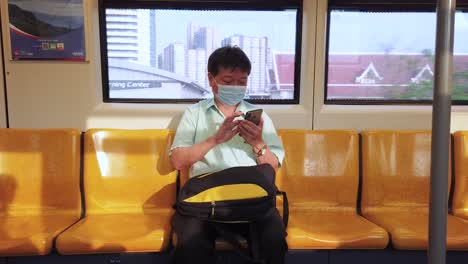 Foto-De-Un-Hombre-Tailandés-En-El-Metro-De-Bangkok-Mirando-Su-Teléfono-Con-Edificios-En-La-Parte-De-Atrás,-Tailandia