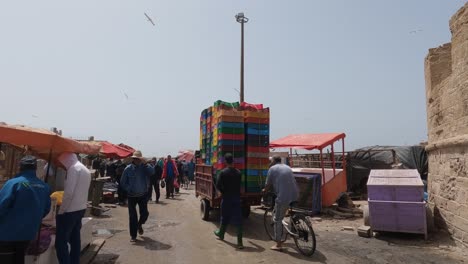 Small-truck-driving-through-busy-market-in-Essaouira,-Morocco