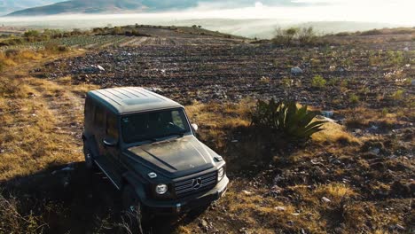 Descenso-De-Drones-Al-Auto-Mercedes-benz-Clase-G-Parado-En-La-Cima-De-Una-Montaña-Desértica