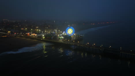 Disparo-De-Un-Dron-Acercándose-A-La-Brillante-Noria-En-El-Muelle-De-Santa-Mónica,-Hora-Azul-En-Los-Ángeles,-EE.UU.