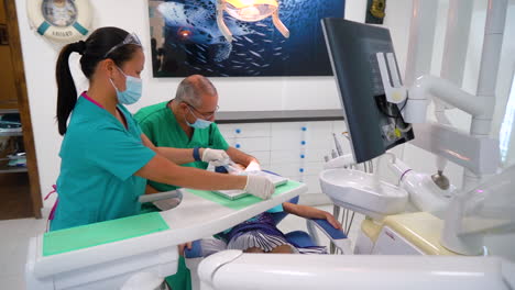 Dentista-Preparándose-Para-Inspeccionar-Los-Dientes-De-Una-Niña-Con-La-Enfermera-Ajustando-El-Equipo