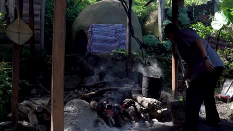 Hombre-En-La-Cabaña-Del-Pueblo-Hirviendo-Agua-En-Cubos-De-Metal-En-Una-Hoguera-Humeante,-Plano-Medio