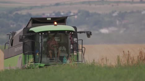 Shot-of-a-green-combine-harvest-working-in-distance-harvesting-wheat-on-a-bright-sunny-day