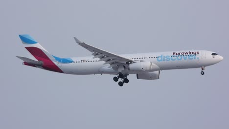 Eurowings-plane-prepares-to-land,-landing-gear-down,-against-overcast-sky