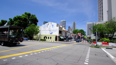 Straßenkreuzung-In-Singapur-Mit-Auf-Der-Straße-Fahrenden-Fahrzeugen-Und-Einem-Niedrigen-Und-Einem-Hohen-Gebäude