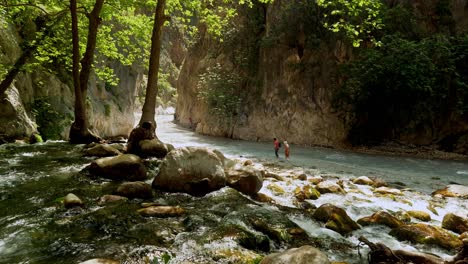 Couple-struggle-to-walk-in-rapid-water-over-rocks-in-Saklikent-gorge-ravine