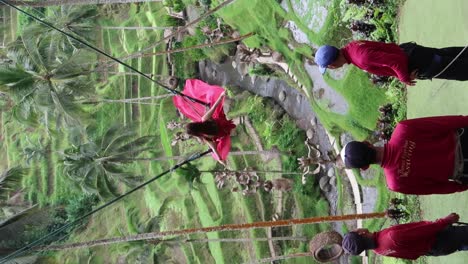 Girl-in-a-long-red-pink-train-dress-getting-a-photo-shoot-riding-swing-over-rice-fields-terraces-in-Alas-Harum,-Ubud-Bali