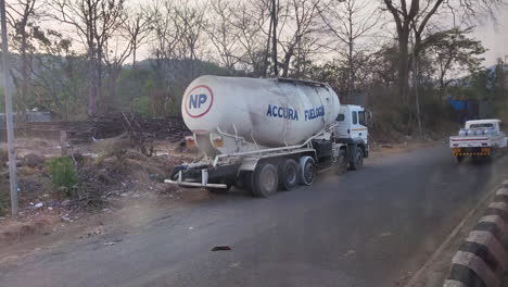 Un-Camión-De-Combustible-Está-Estacionado-Al-Costado-De-La-Carretera,-Su-Imponente-Presencia-Enfatizada-Por-Los-Vehículos-Que-Pasan-Al-Fondo-|-Transporte,-Combustible,-Inflamable,-Camión