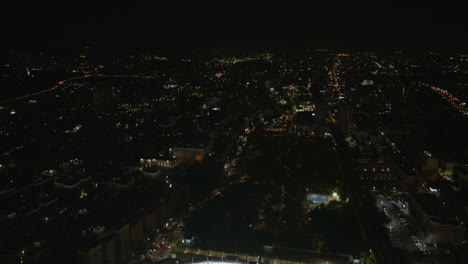 Aerial-view-tilting-over-the-Yankee-stadium,-revealing-the-Concourse-cityscape,-night-in-NY,-USA