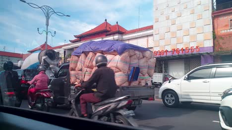 Beobachten-Sie-Den-Pendlerverkehr,-Motorroller,-Autos-Und-Lastwagen-Auf-Den-Stark-Befahrenen-Straßen-In-Bali,-Indonesien,-Aus-Der-Sicht-Eines-Taxis