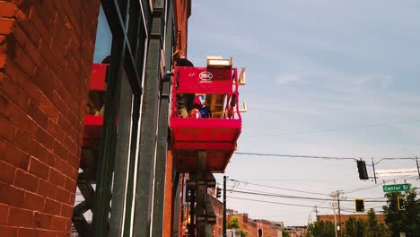 Dos-Hombres-Reparan-Ventanas-En-Lo-Alto-De-Un-Ascensor-Mecánico.