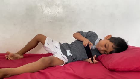 Un-Niño-Asiático-De-4-Años-Jugando-En-Su-Teléfono-Inteligente-Mientras-Está-Acostado-En-La-Cama