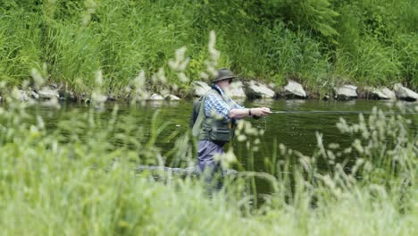 Un-Hombre-Con-Sombrero-Y-Gafas-De-Sol-Se-Encuentra-En-El-Río,-Dedicado-Al-Arte-De-La-Pesca-Con-Mosca