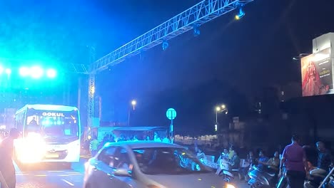 Filmischer-Ruß,-Nachts-Spielt-Eine-Live-Musik-Festivalkonsole-Auf-Der-Straße-Und-Viele-Fahrzeuge-Fahren-Durch-Die-Straße