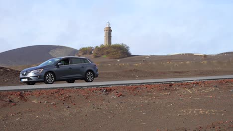 Coche-Detenido-Con-Luces-De-Advertencia-En-Capelinhos-Paisaje-Volcánico-Con-Faro-En-El-Fondo,-De-Mano