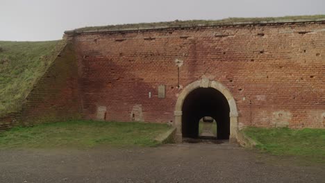 Primer-Plano-De-La-Antigua-Pared-De-Ladrillo-De-La-Fortaleza-De-Terezín-Con-Una-Pequeña-Entrada-Arqueada,-Rodeada-De-Hierba-Y-Un-Cielo-Despejado.