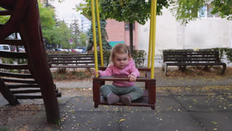 Happy-young-girl-with-blond-hair-swinging-on-park-swing,-wide-angle-front-view