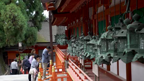 Reihe-Hängender-Laternen-Am-Kasuga-Taisha-Schrein-Mit-Einer-Gruppe-Japanischer-Besucher,-Die-Im-Hintergrund-Beten