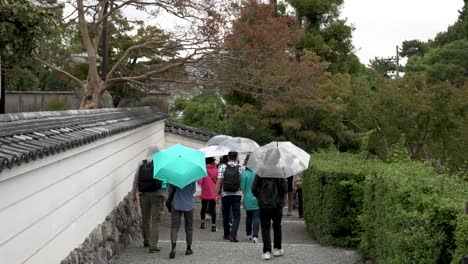 Tourists-Holding-Umbrellas-Walking-Along-Path-At-Byodo-In-Temple-Grounds-In-Uji,-Japan