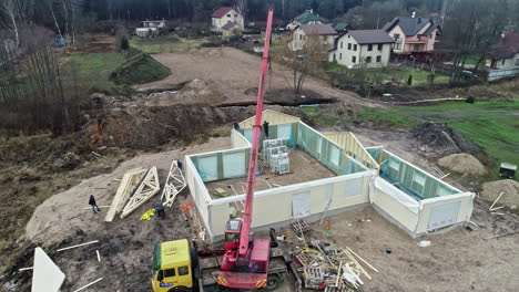 Aerial-view-circling-a-crane-at-a-private-house-construction-site,-cloudy-fall-day